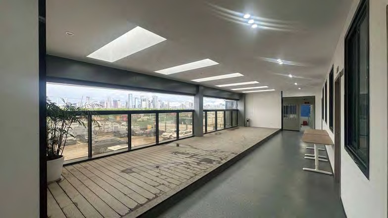 Indoor viewing terrace with a raised timber deck, continuous dark-framed glazing along one wall and a flat ceiling with recessed lights